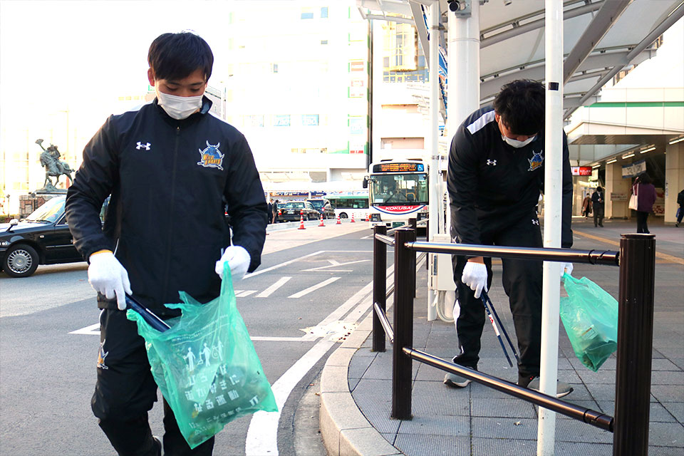 画像：ゴミ袋とトングを手に道端に落ちているゴミを拾う新井選手、新妻選手