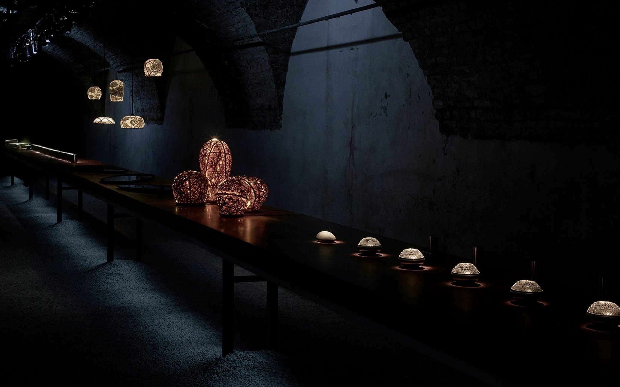 暗い室内に並ぶ照明器具と装飾品、アーチ型天井と煉瓦壁のある空間