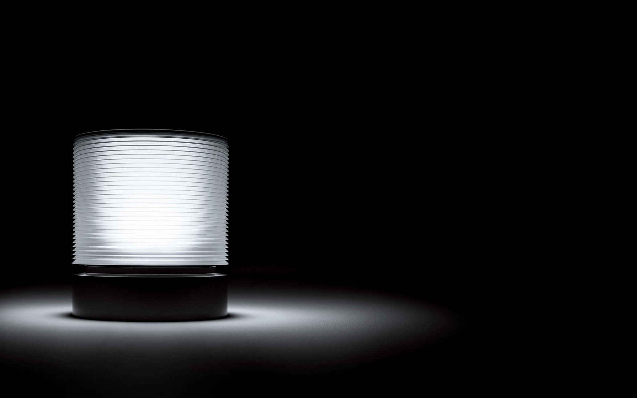 日本語のALT：黒背景に白く光る円筒形の照明器具とその光の反射