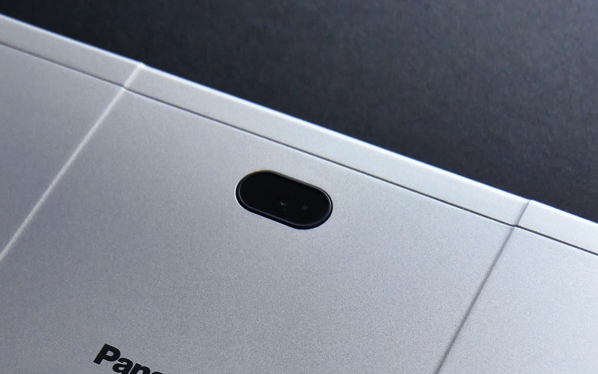 シルバー色のノートパソコンの上部中央に位置するカメラ部分、背景は暗色の机面