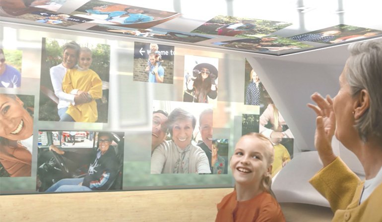 室内ガラス窓に複数の人物写真が貼付けられ、手を挙げて話す人物が室内にいる様子