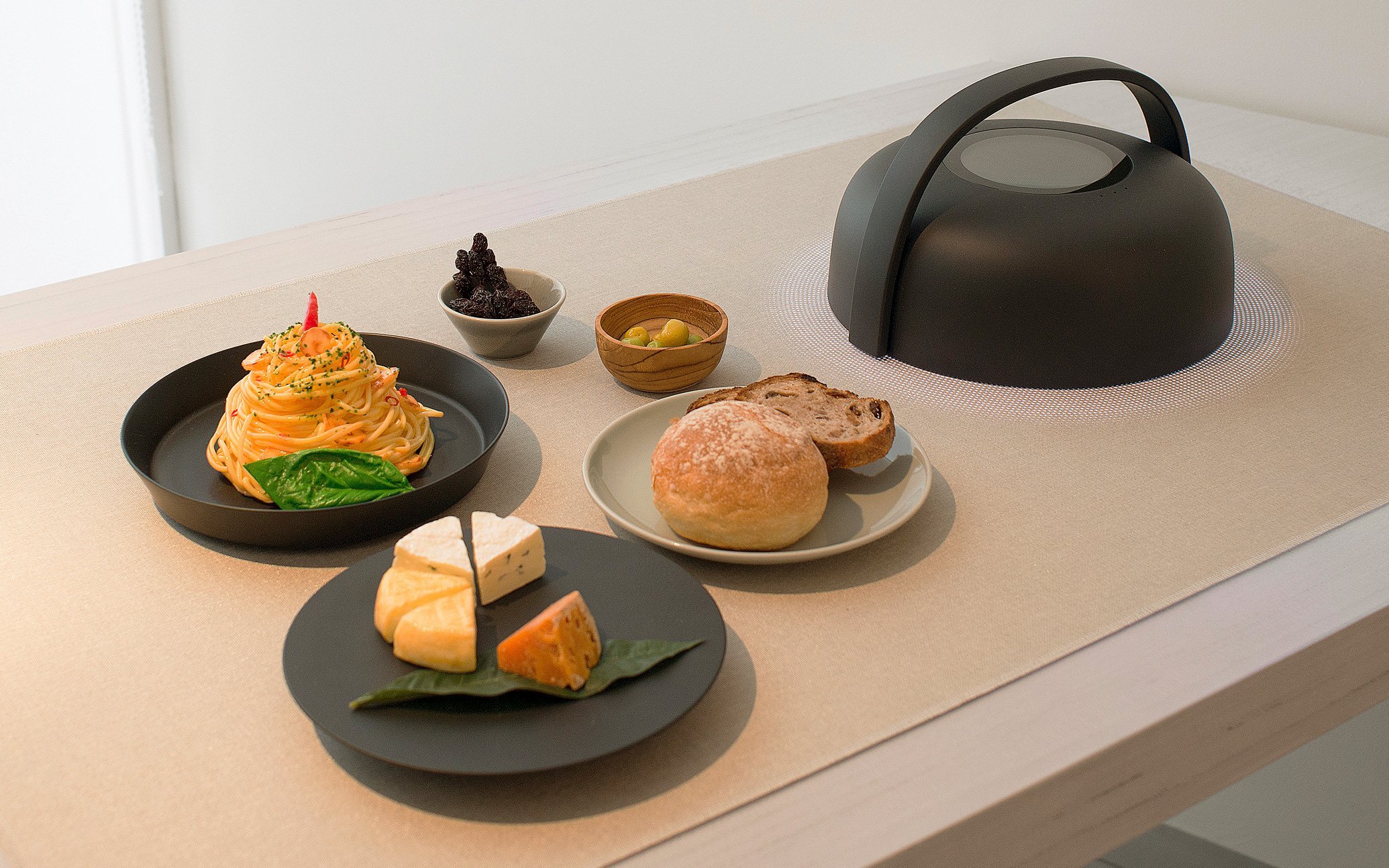 白い木製テーブルの上にパン、パスタ、チーズ、果物、デザートと黒い電気ケトルを配置した食事の風景