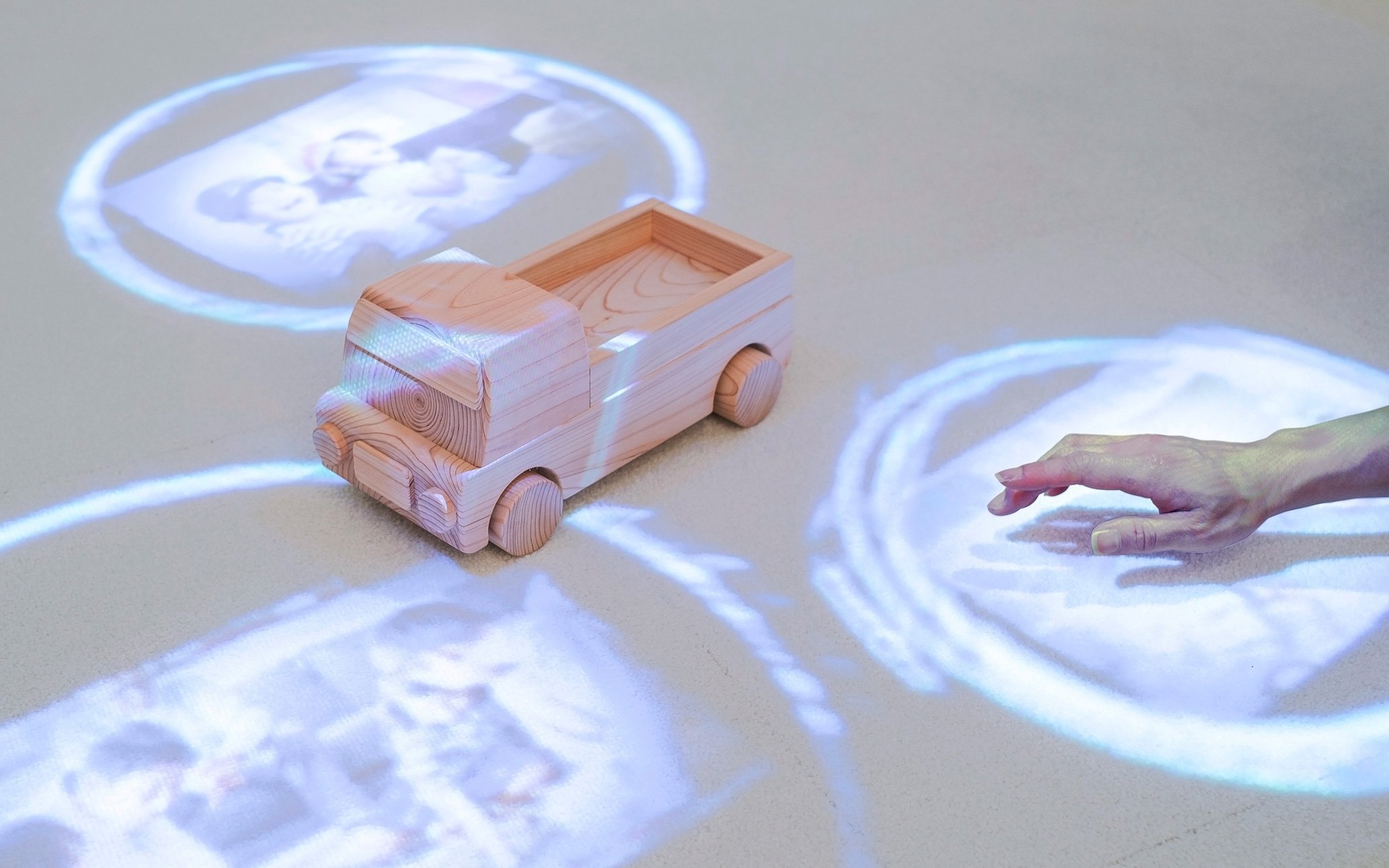 木製の玩具トラックの上に映像が投影され、手が映像の中に触れている様子