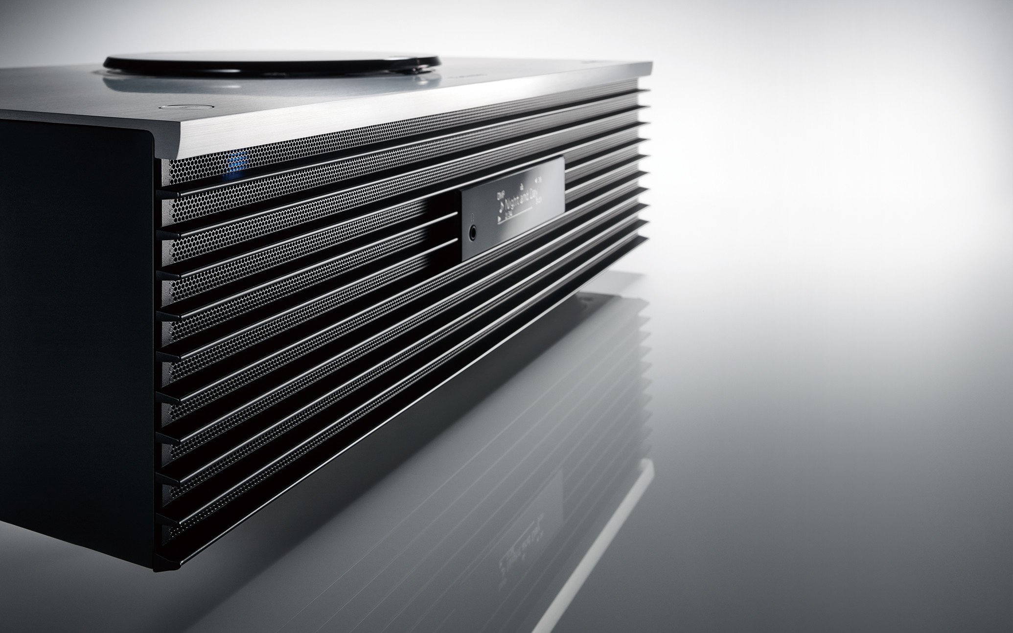 天面に搭載されたシルバーのCDプレーヤーで、正面は黒のスピーカーで中央に小さめのディスプレイを備えるデザイン