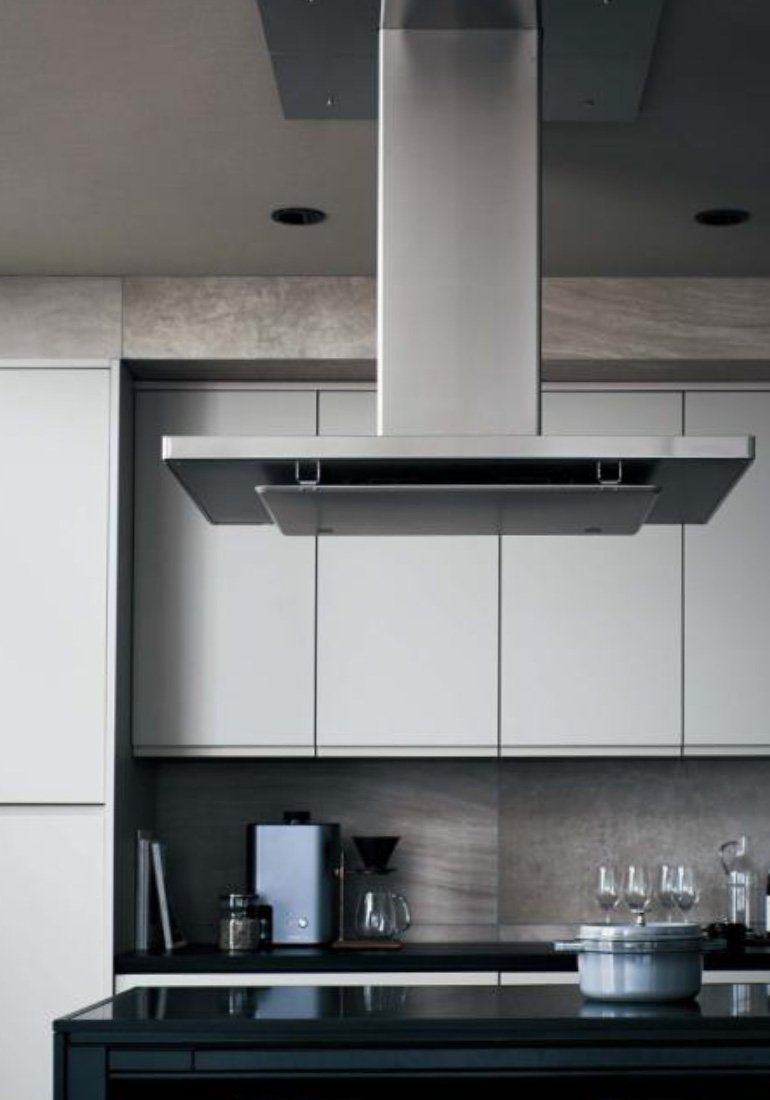ステンレス製のレンジフードが取り付けられたモダンなキッチン。白いキャビネットと黒いカウンター、コーヒーメーカーやガラスのコーヒードリッパー、鍋が置かれたコンロ。
