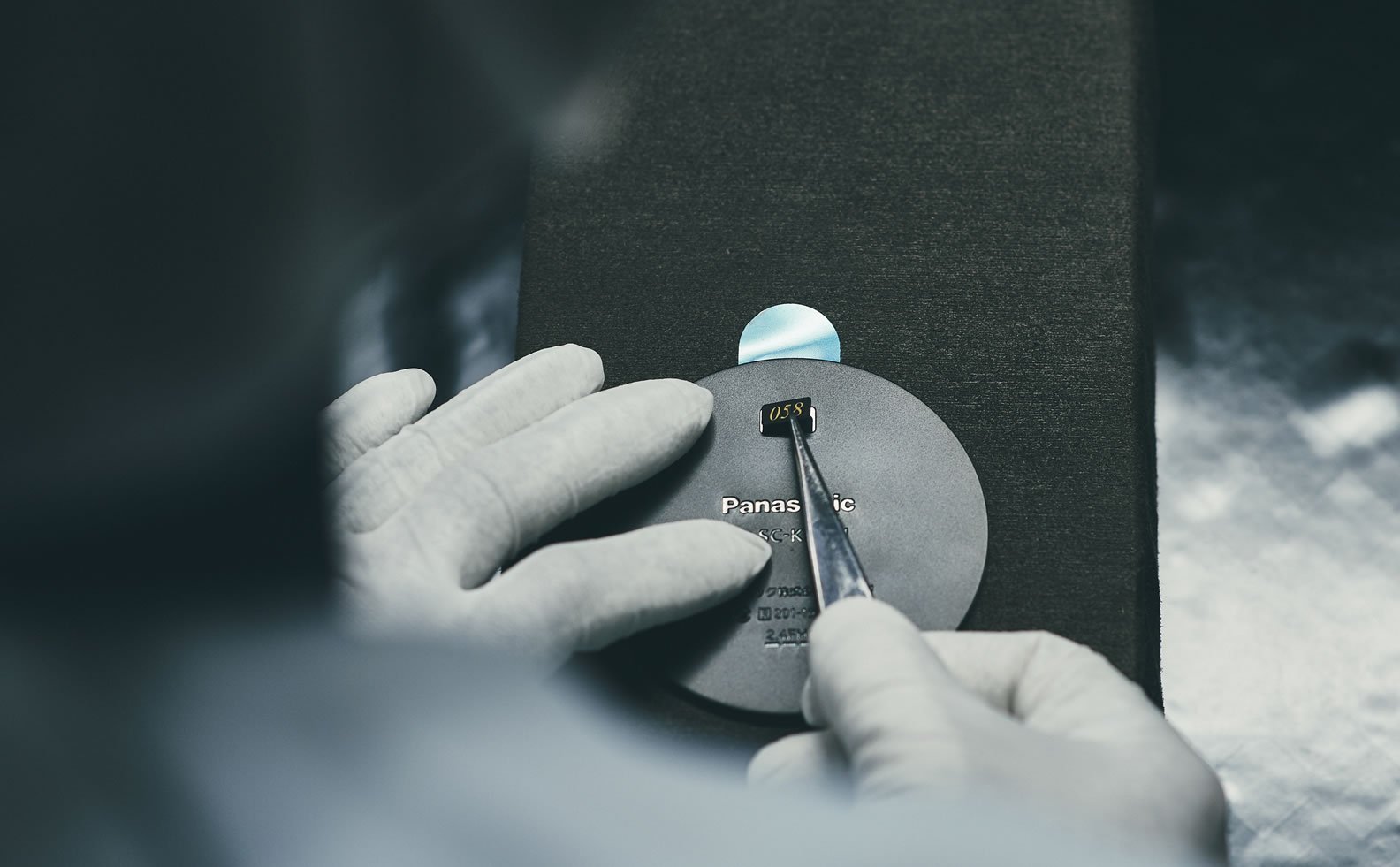 茶筒型スピーカーにシリアル番号のプレートを装着、手袋をした作業者