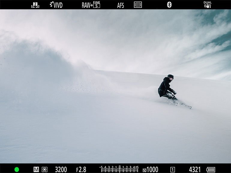 雪原を滑るスキーヤーのシルエットと広がる青空の風景をのぞく、カメラのファインター画面