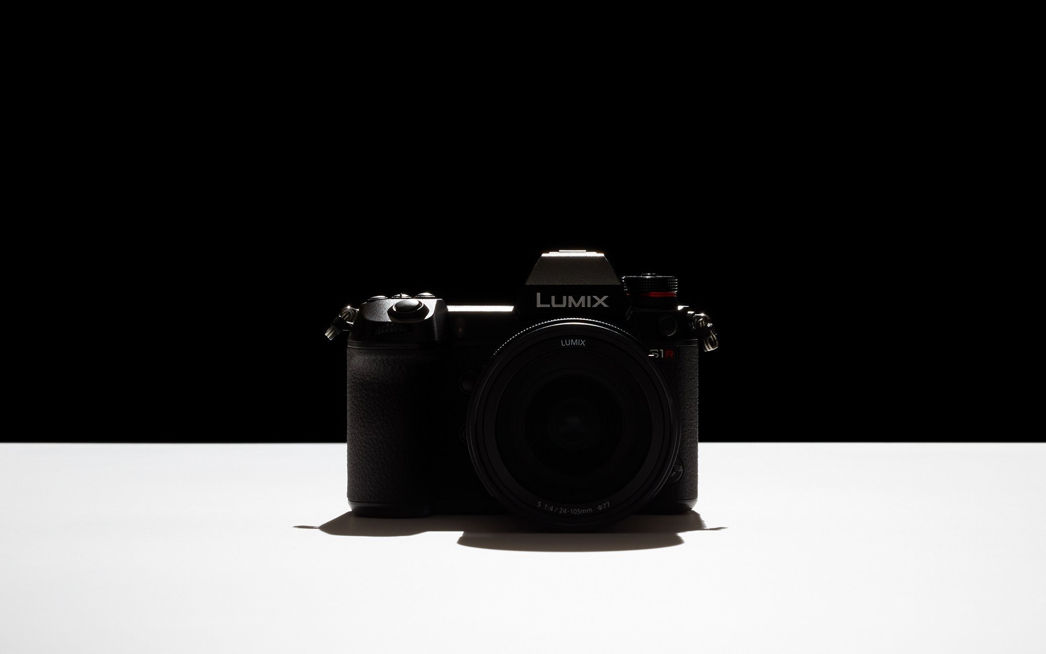 カメラ本体のシルエット　白い卓面に上から強い光が当たり、本体はシルエットのみ浮かび上がっている