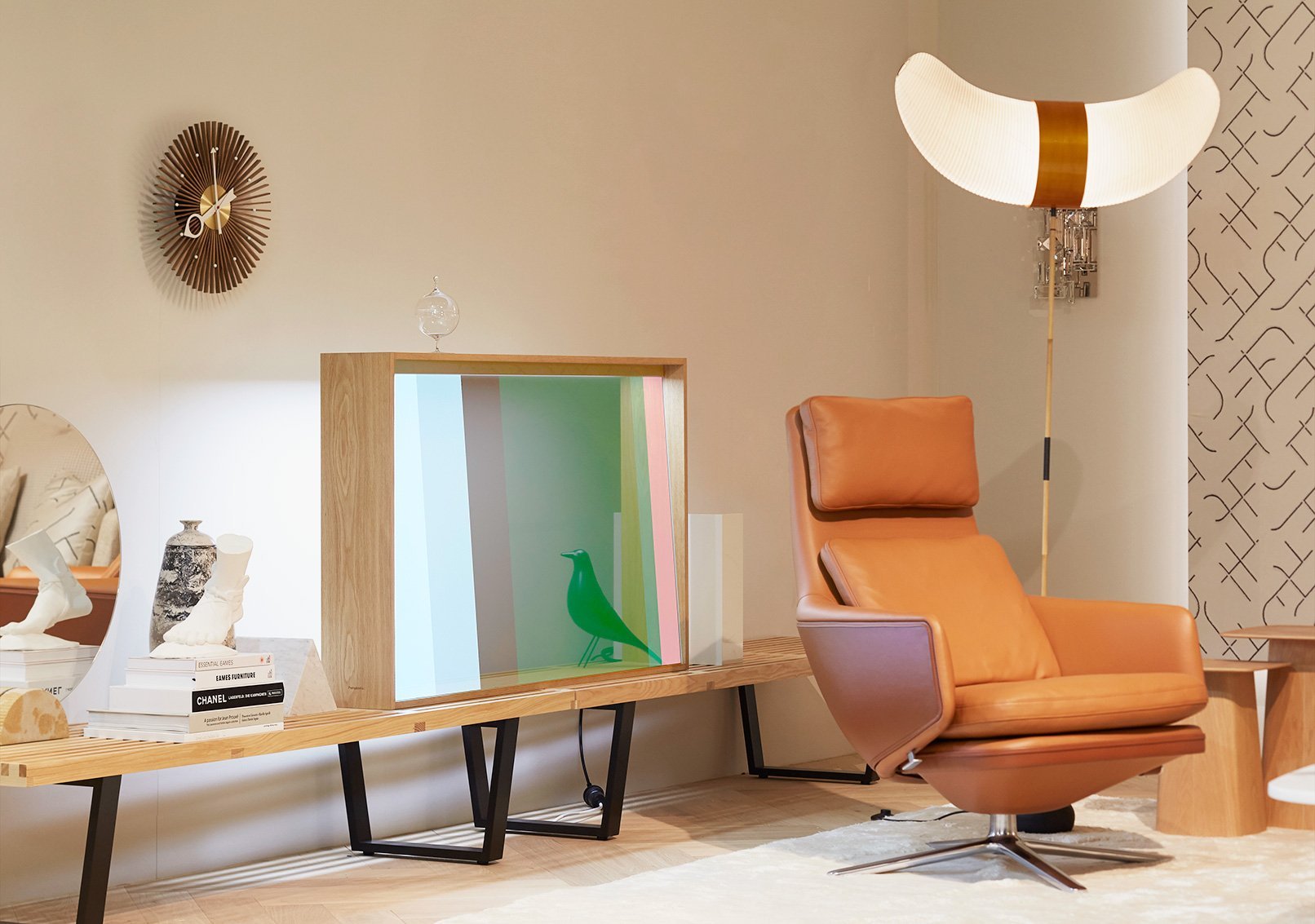 木製フレームの透明ディスプレイと茶色のリクライニングチェア、壁に掛かる月形の照明と丸い壁掛時計、サイドに棚と装飾品