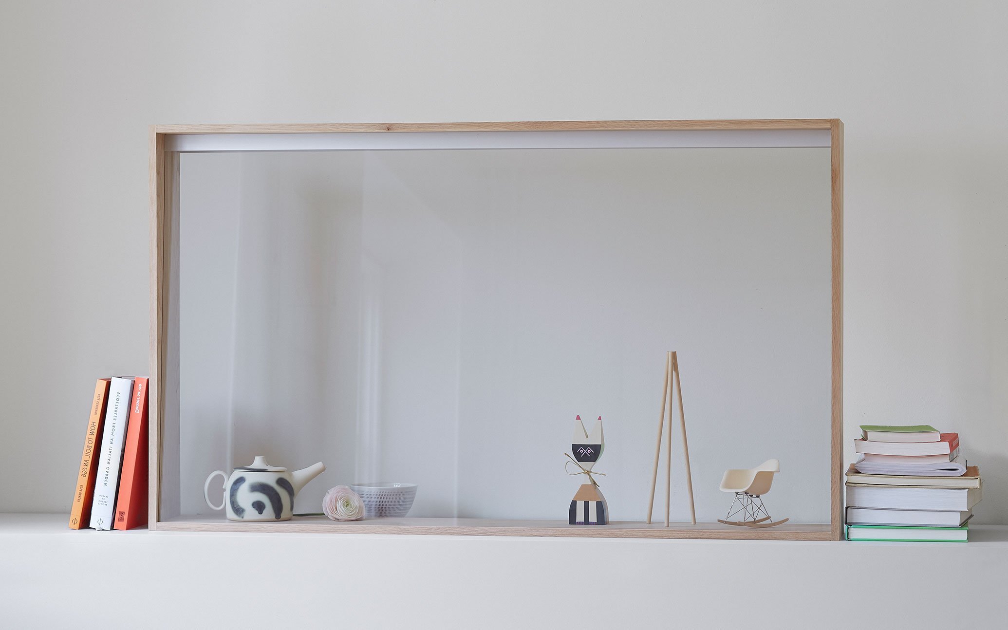 木製フレームの透明ディスプレイの向こうに積み重ねられた本、陶器のポット、木製の人形、ミニチュアの椅子、左右に本の配置