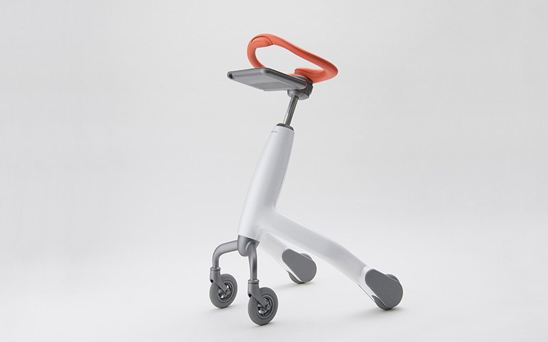 白を基調とした歩行トレーニングロボット。3輪構造で、オレンジ色のハンドル、グレーのタブレット取り付け部、白い本体。グレーのキャスターホイール付き。白い背景での撮影