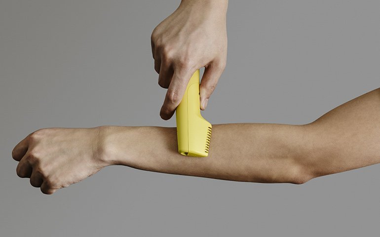 黄色の電気シェーバーが腕に当てられ、操作されている様子のアップ画像  