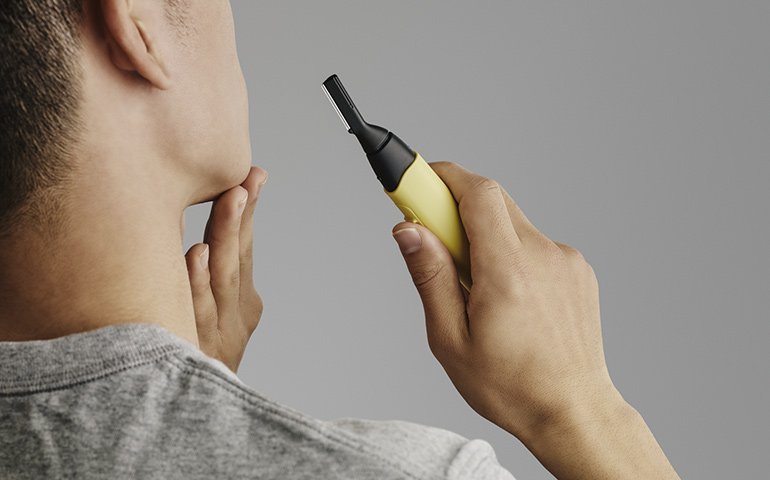 グレーのシャツを着た男性が黄色の鼻毛カッターを鼻に近づけている様子  