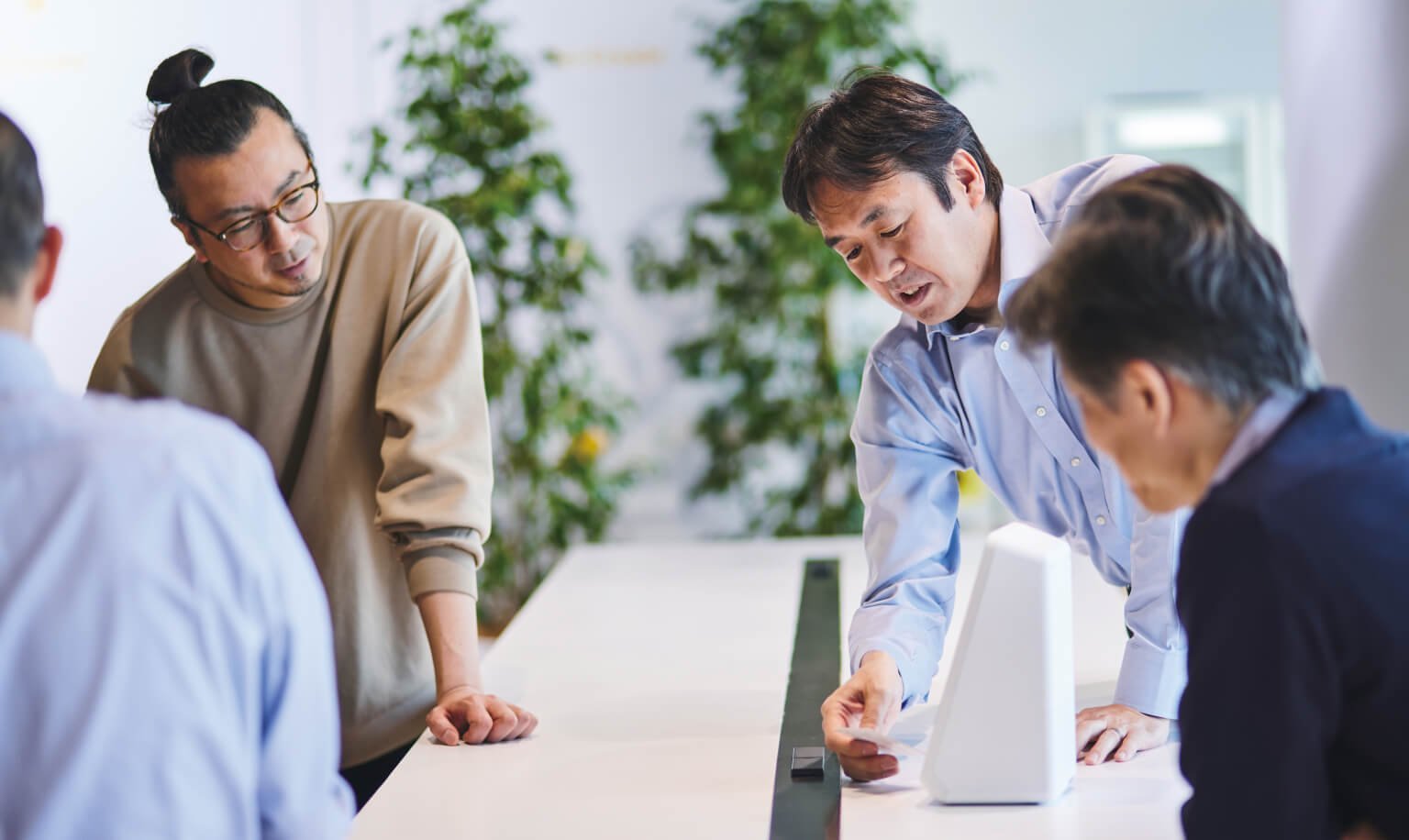 会議で議論する四人のビジネスマンの姿。カードリーダー端末にカードを入れながら説明している様子。