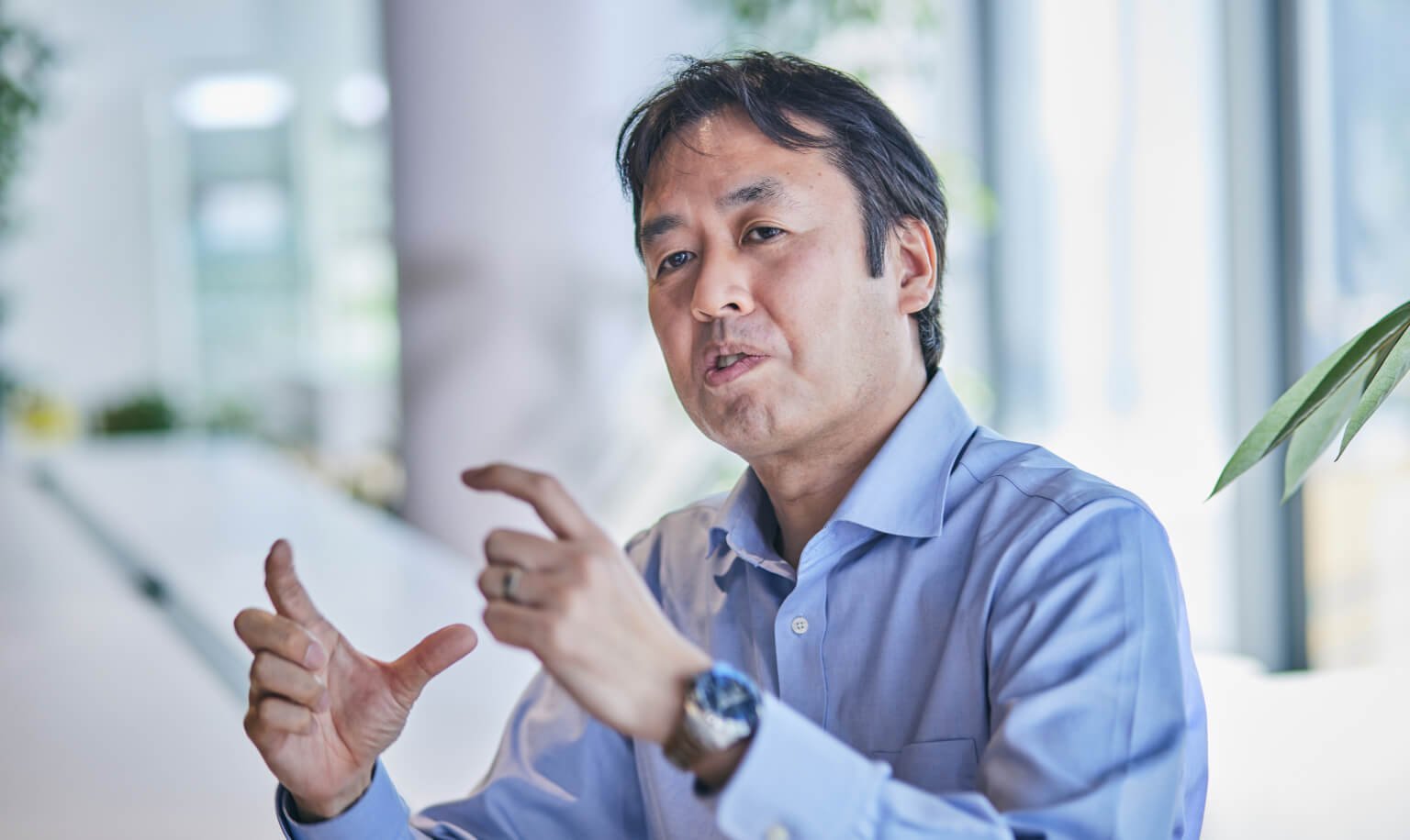 青色のシャツを着た男性が、手を広げて話す姿