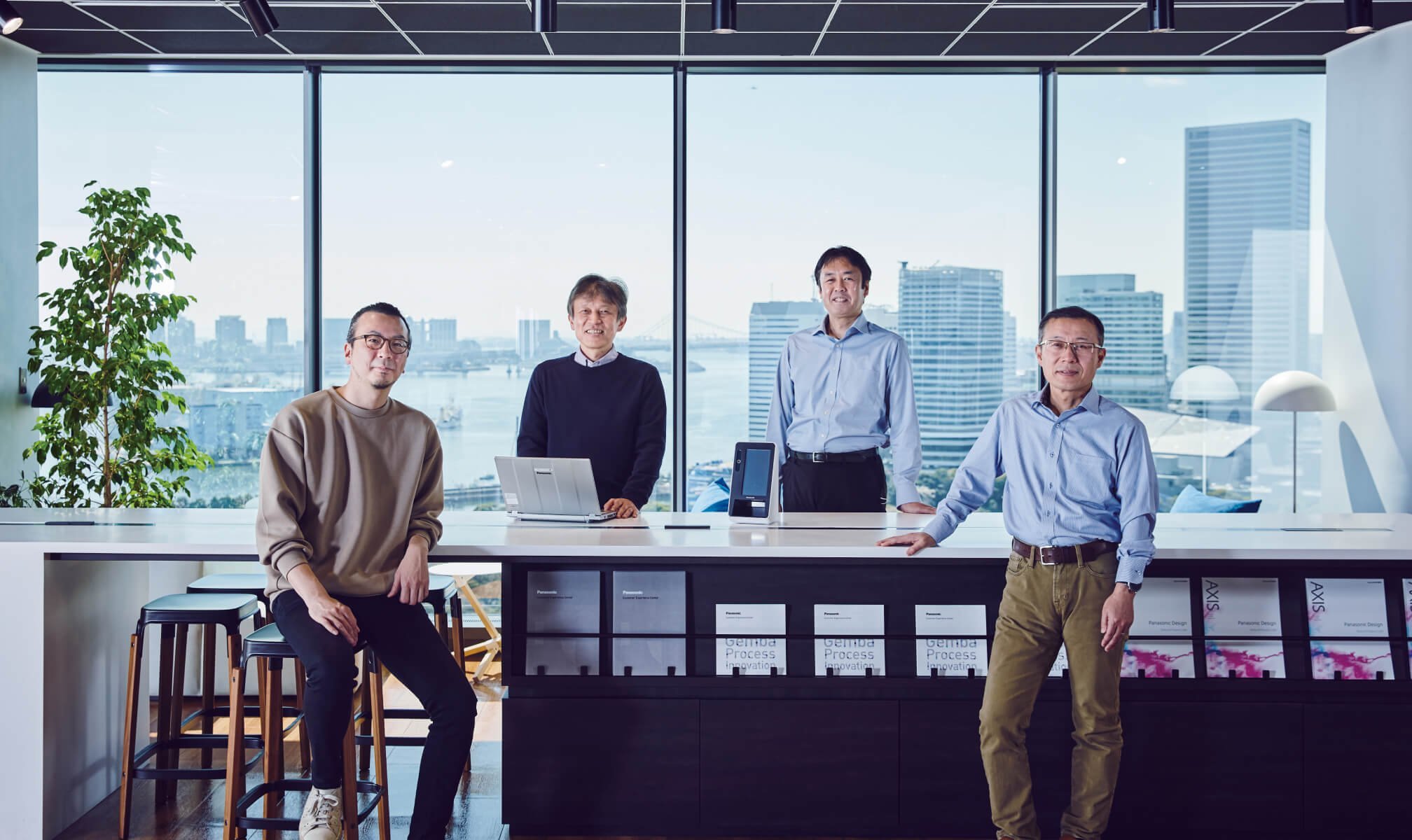 開発に関わった四人が会議室で正面を向いて並んでいる、中央にノートパソコンとカードリーダー端末機がある