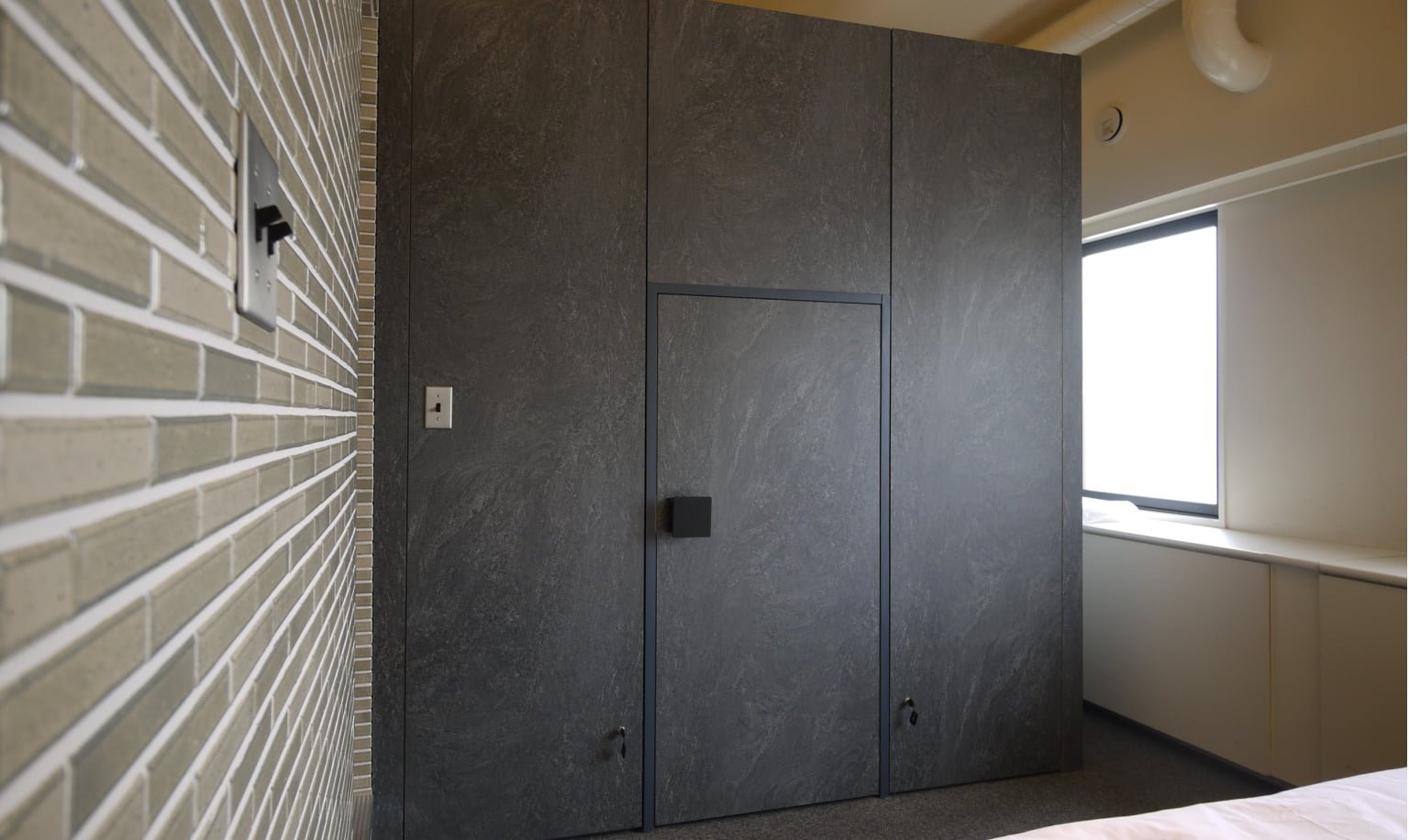 一面ホテルの一室の正面位、一面茶色の壁がある。扉が区切られている　手前にベッドが見えている