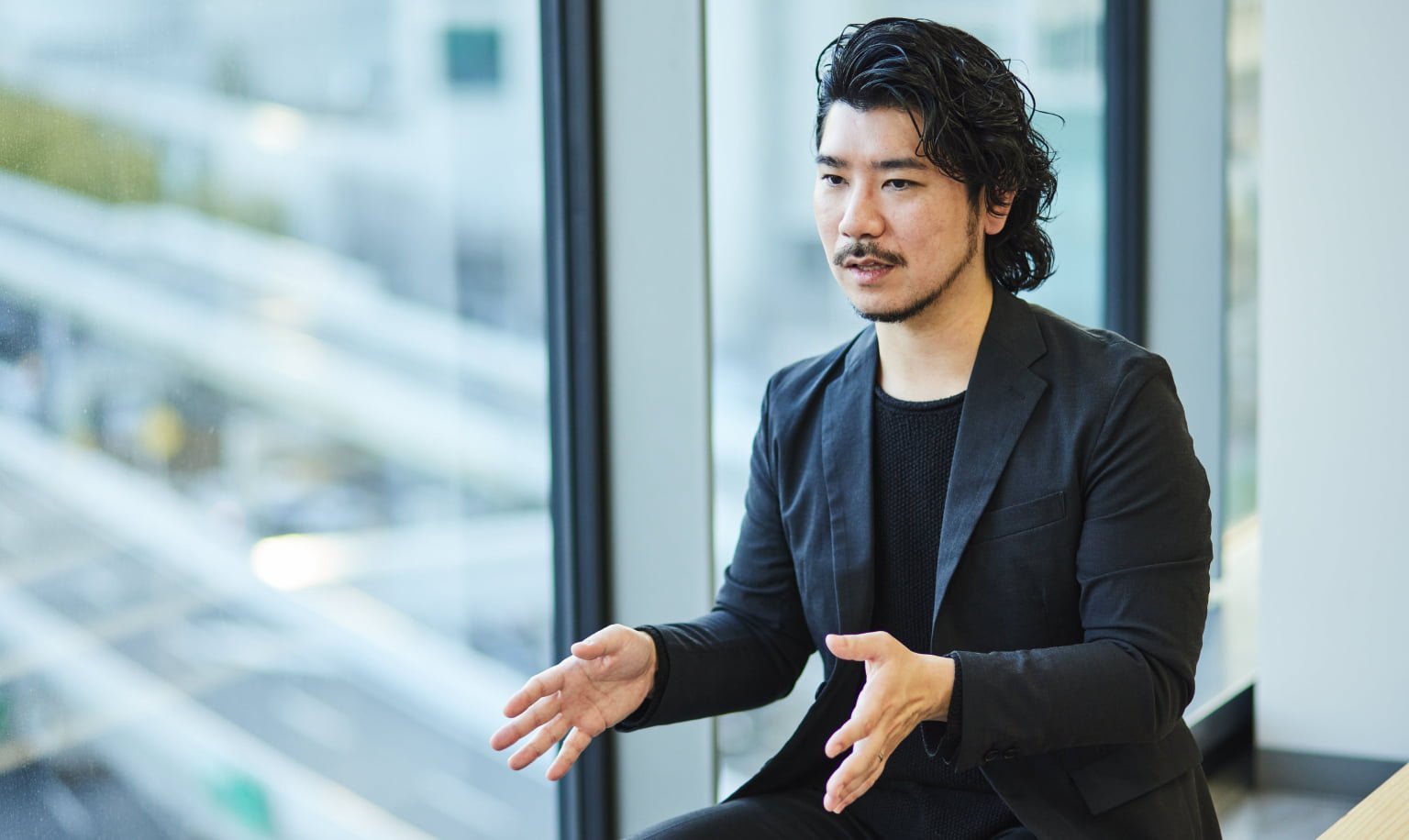 黒い服を着た男性が手を広げながら話している様子