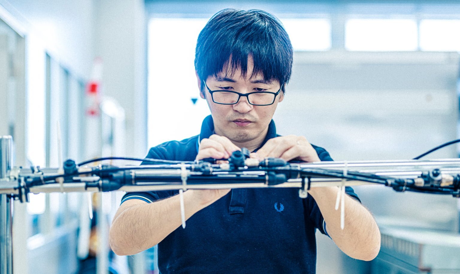 ネイビーのポロシャツを着て眼鏡をかけた男性（田端）がメカを扱っている様子を正面から捉えた画像