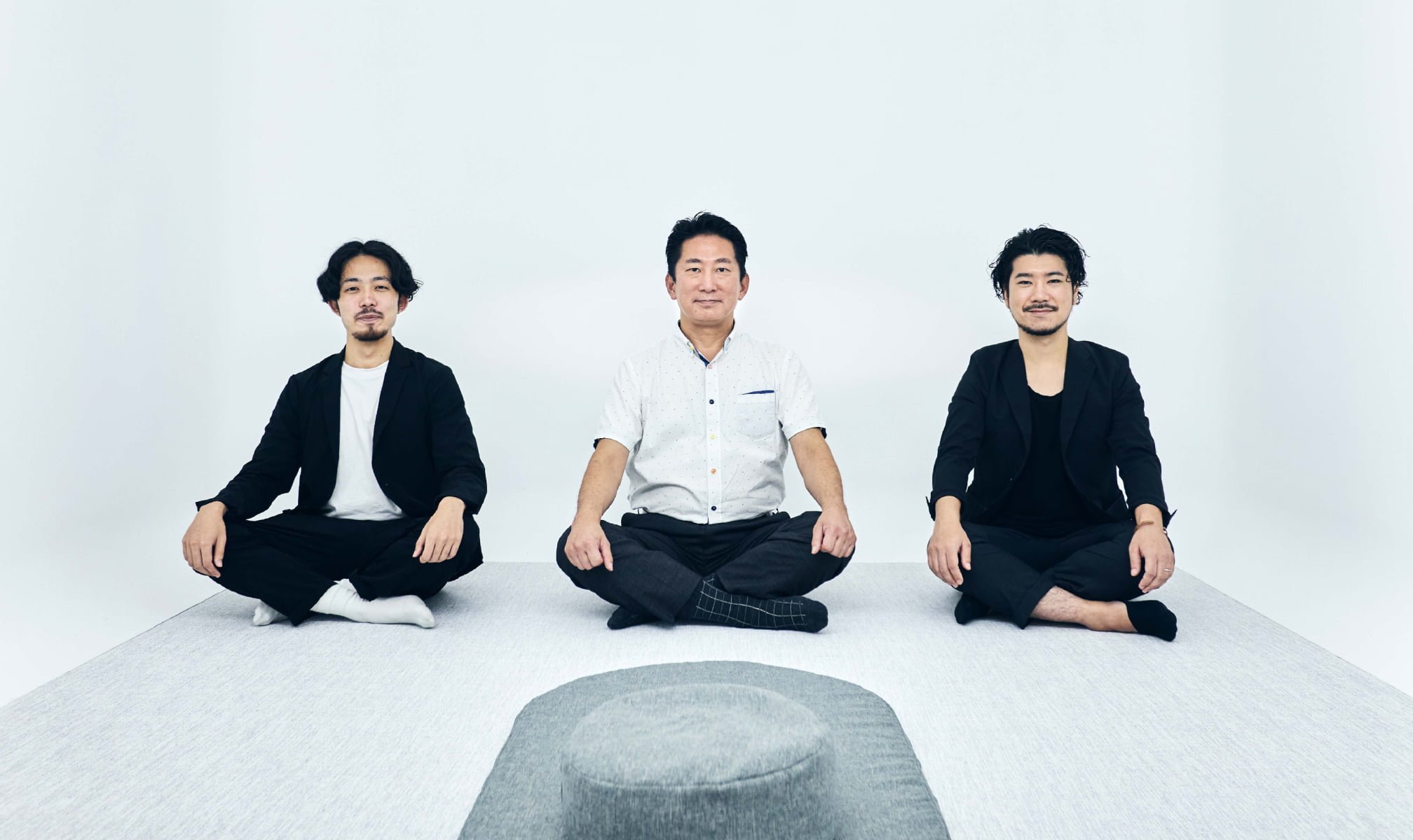 白い空間に3人の男性が胡座をかいて座っている