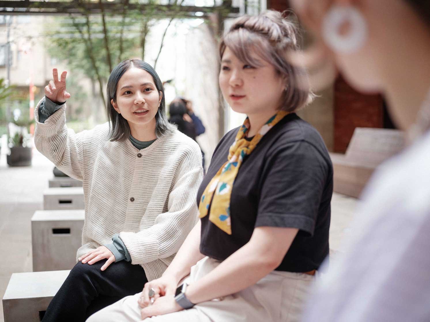 ベンチに座る三人の人物が手振りを交えて会話している様子