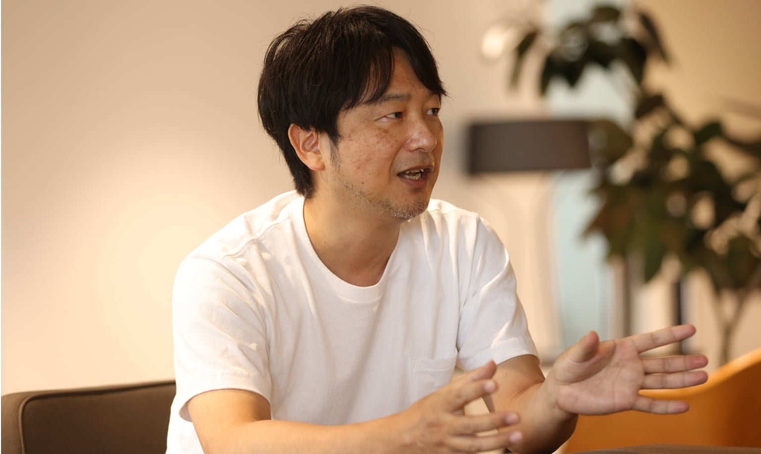 白いTシャツを着た男性がテーブルの前で手を動かしながら話している