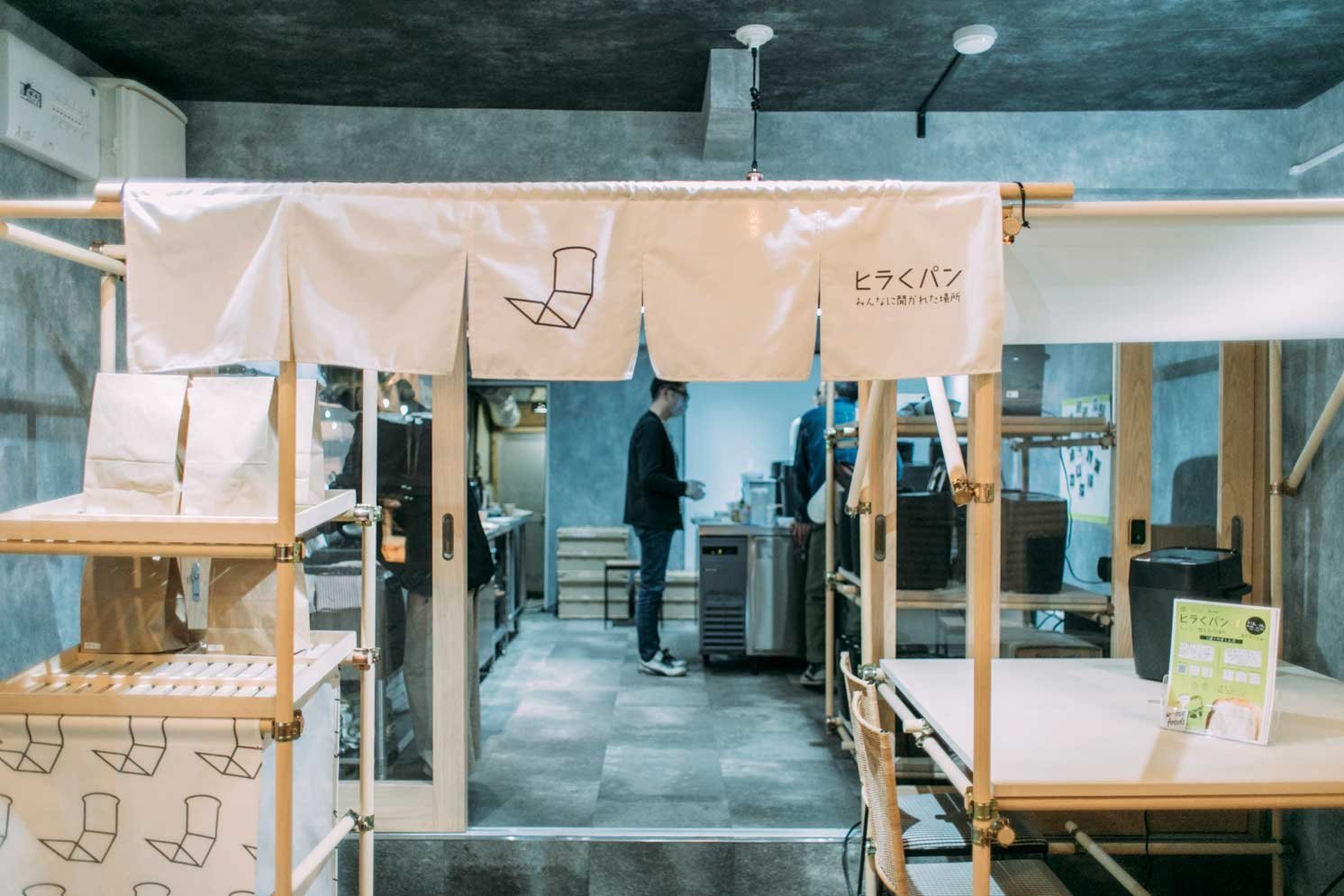 暖簾に「ヒラクパン」と書かれた店舗入口と奥の厨房スペース
