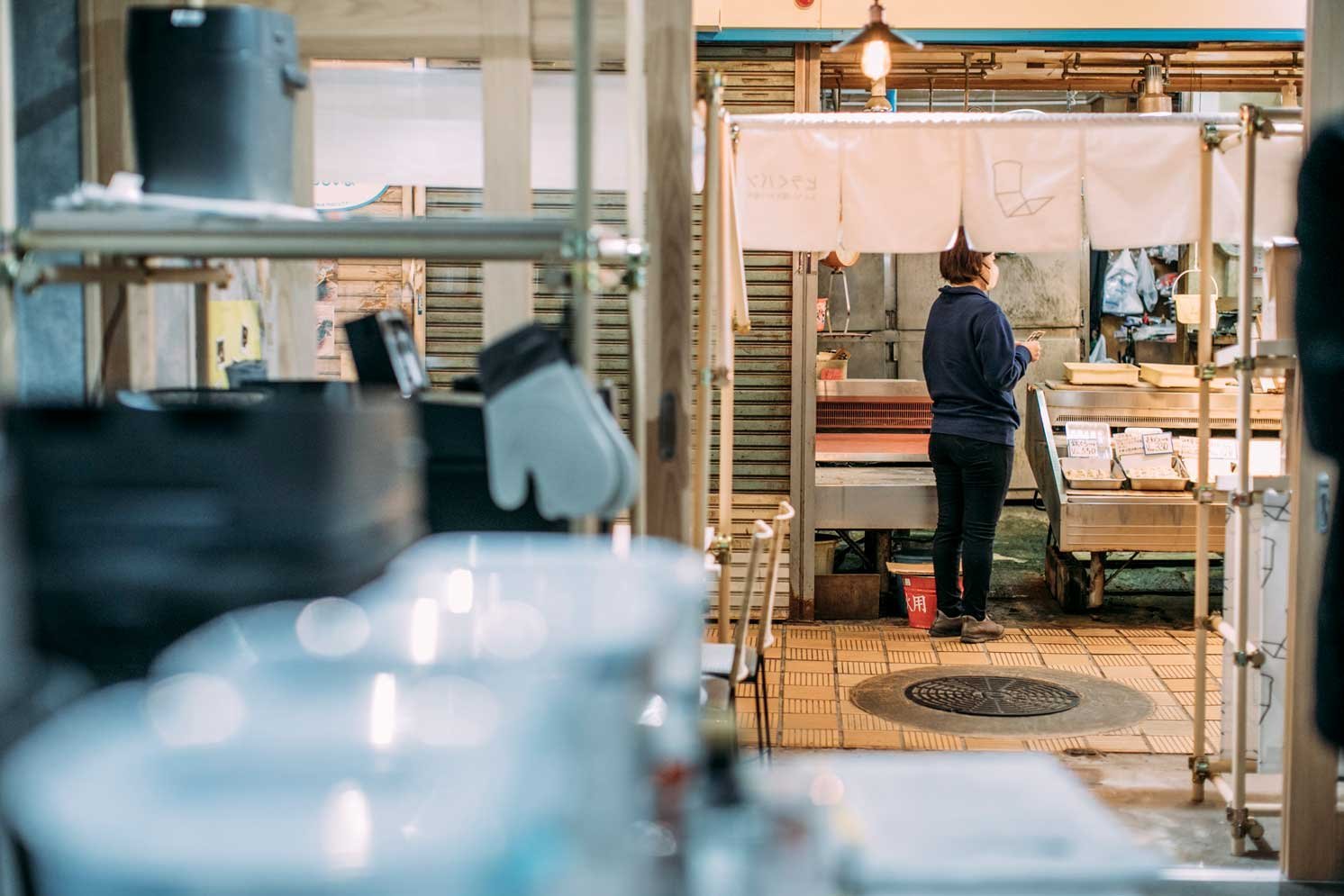 店内カウンター越しに立つ人物と、調理台や器具が並ぶ様子