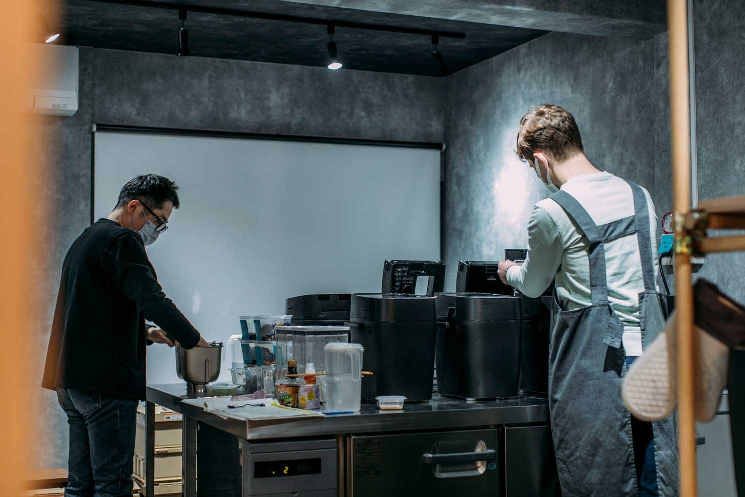 室内の作業台で調理器具を扱う二人の人物