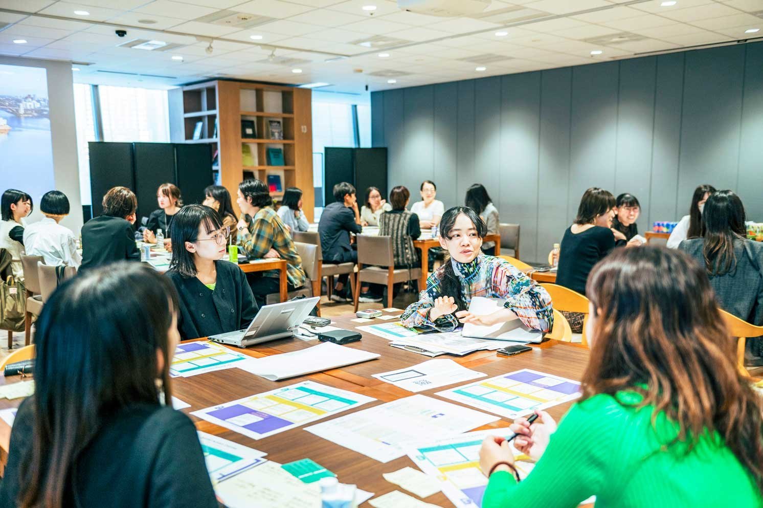 資料とノートパソコンを広げ、テーブルで議論する複数の人物