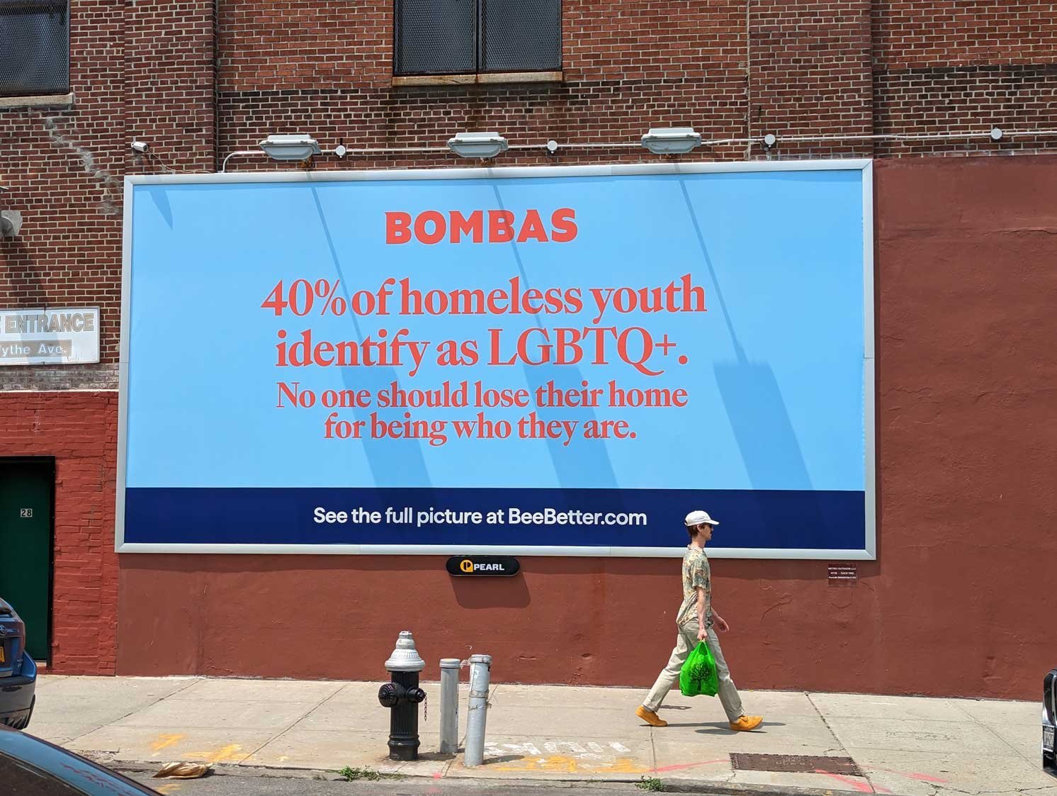 レンガ壁に掲出された「BOMBAS」広告看板と歩道を歩く人物