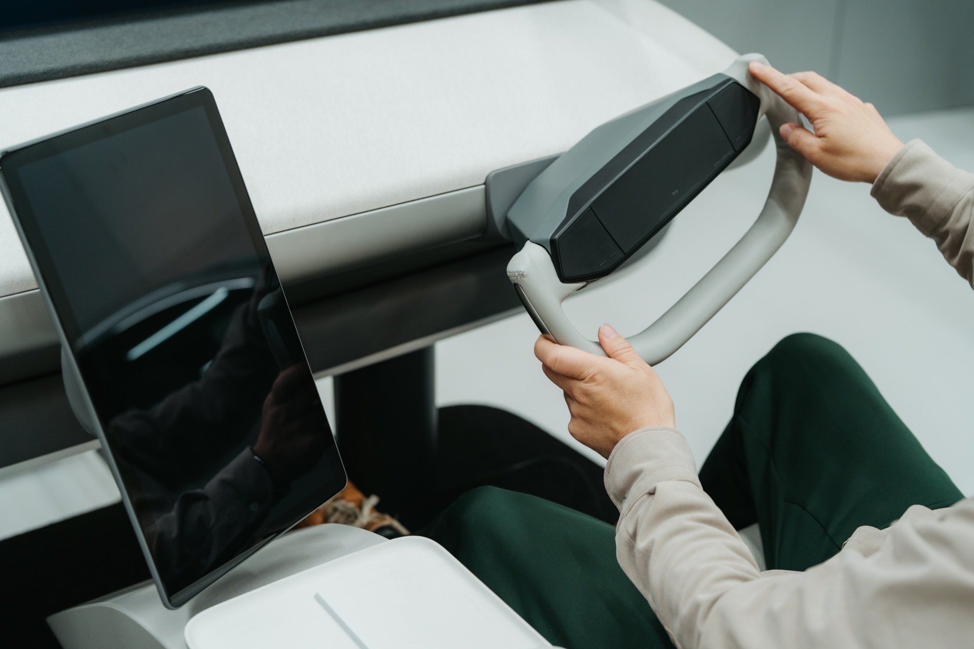 ハンドルを握る人物、タブレット端末が置かれたコンソール、近未来的なデザイン、運転席