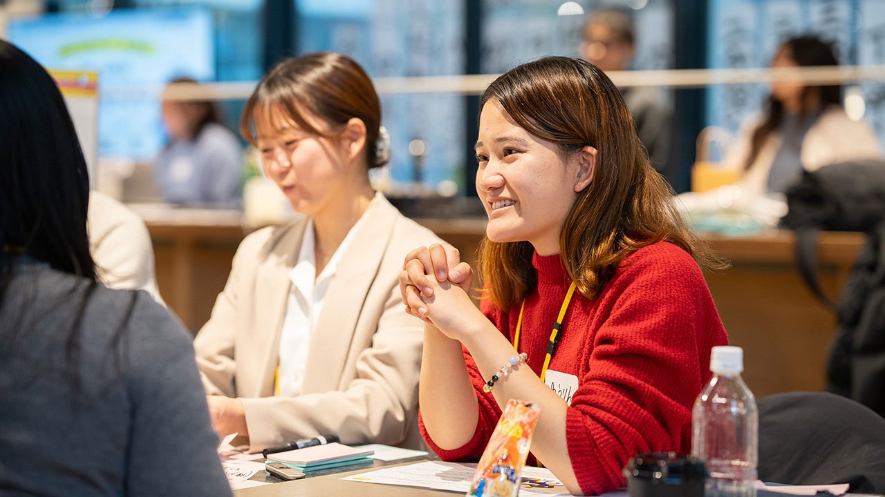 赤いセーターを着た女性と、白いジャケットの女性が対話をしている。