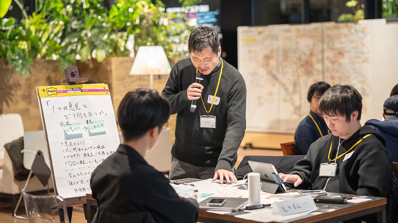 アイデアが書かれたボードの前で、立ち上がってプレゼンをする参加者