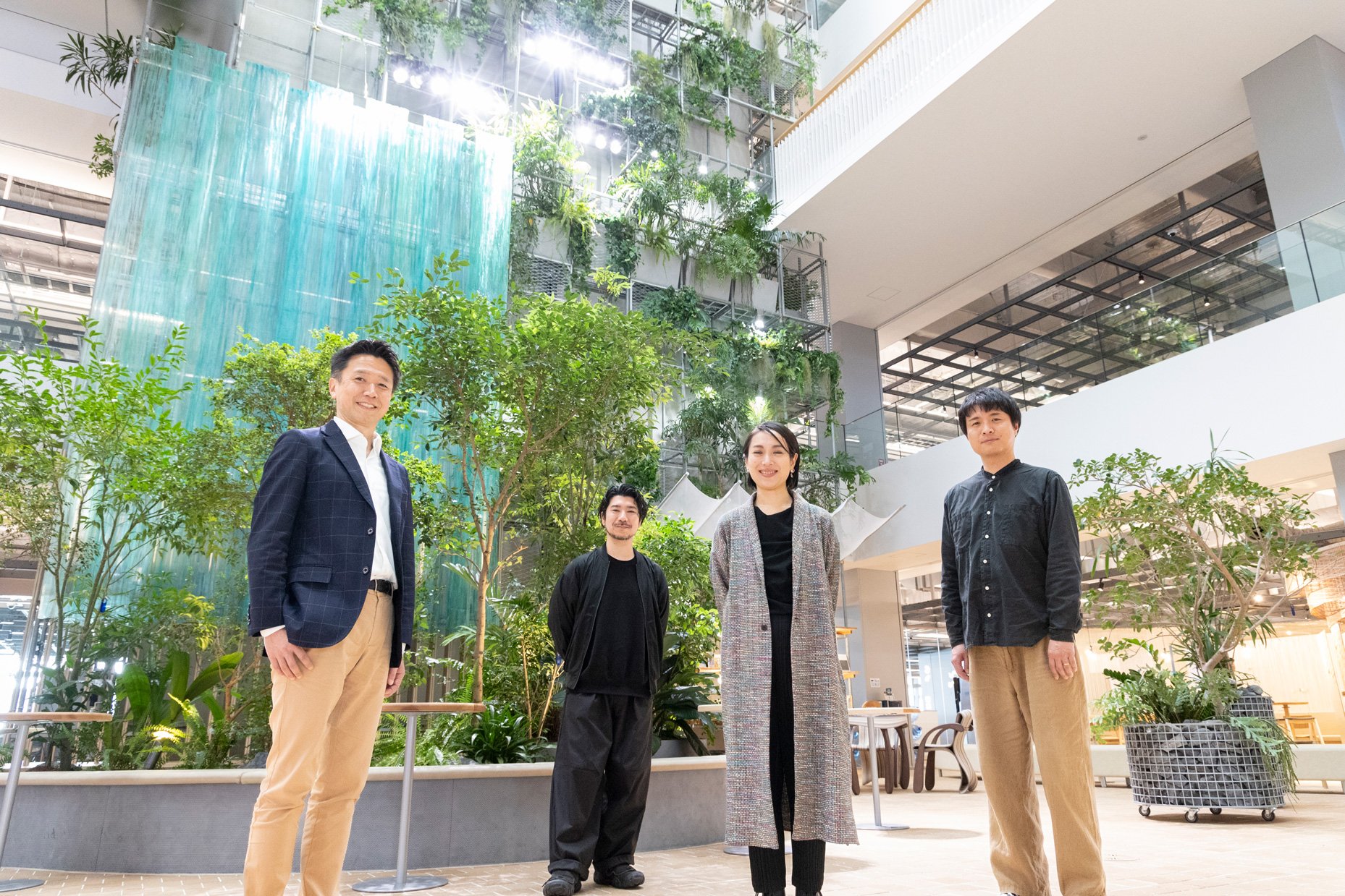 緑の植栽と青い壁を背景に、4人のメンバーが立っている。