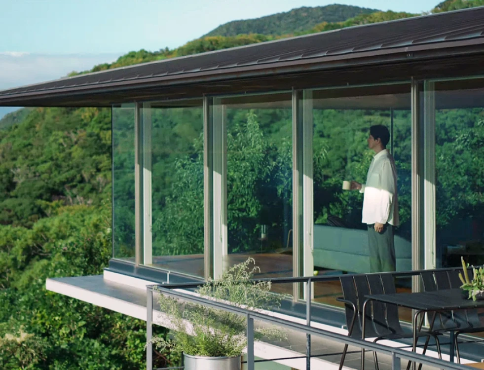 写真：テラスでマグカップを持ち緑の木々を眺める男性