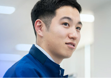 青い制服を着て、横を向きながら微笑む男性