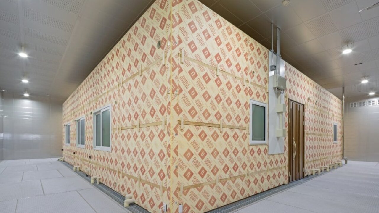 住宅環境を再現した空質空調検証室の外観。ロゴ入りの高性能断熱材で覆われた試験用構造物の様子。