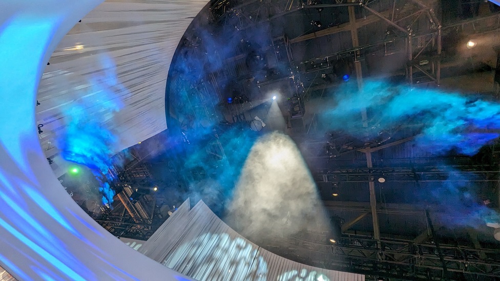 The mist sprayed from a nozzle installed in an oval frame overhead is illuminated by the light of a projector.