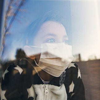 マスク姿の女性が窓の外を眺める画像