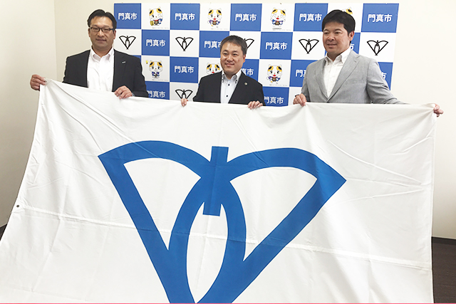 画像：市旗を掲げる脇坂部長、宮本市長と田中監督